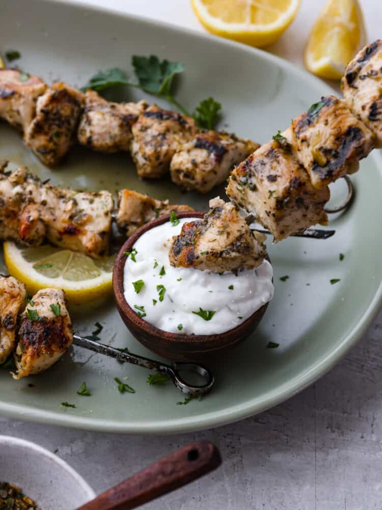 Closeup of chicken souvlaki being dipped in sauce.