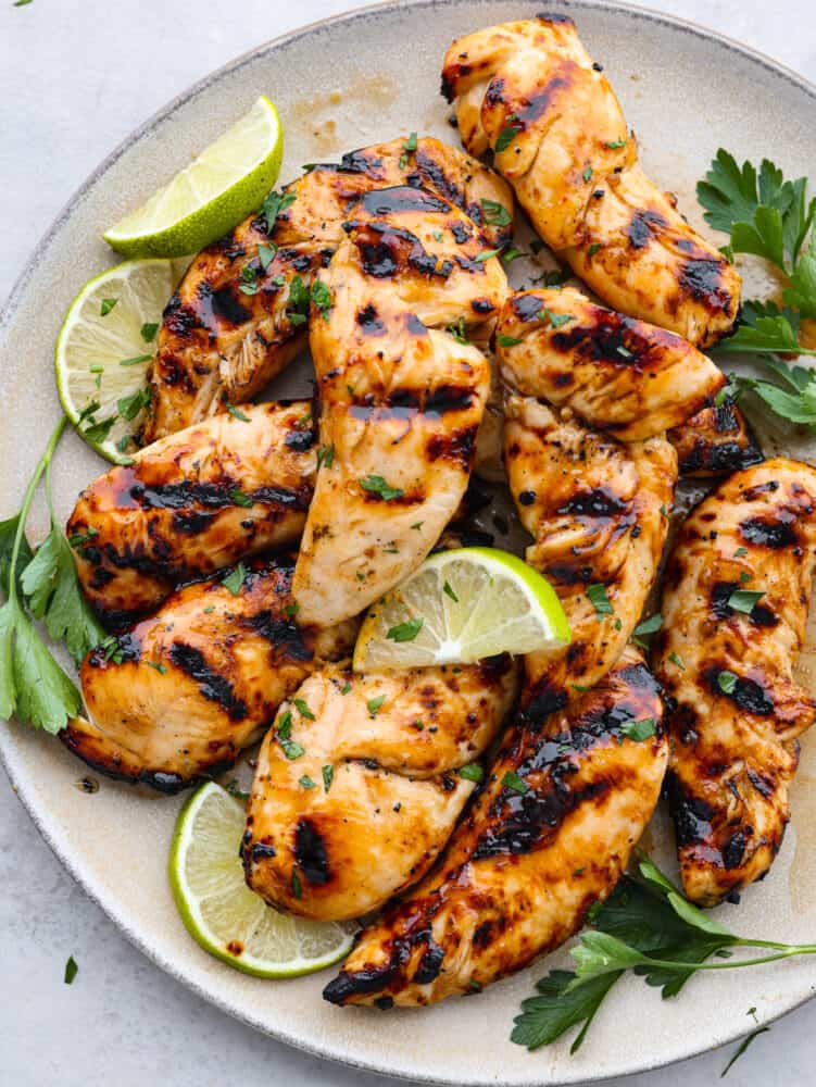 Top-down view of grilled chicken tenders on a gray plate, garnished with lime slices and herbs.