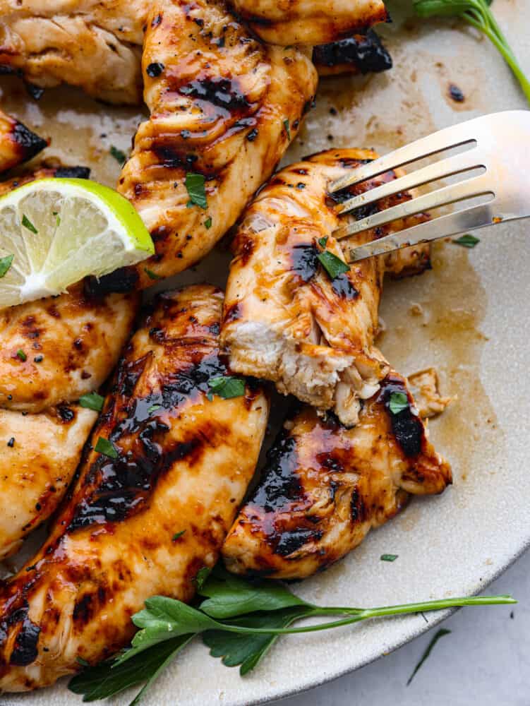 A cut chicken tender being skewered with a fork.