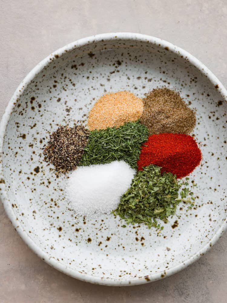 Close up photo of the seasonings and herbs clustered together on a small beige speckled plate.