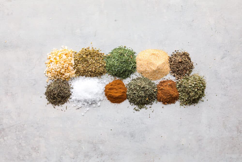 The various spices used in Greek seasoning measured and laid out on a flat surface.