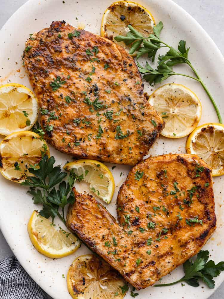 Overhead view of two grilled swordfish steaks on a large white platter. Grilled lemon slices and parsley garnished on the side.