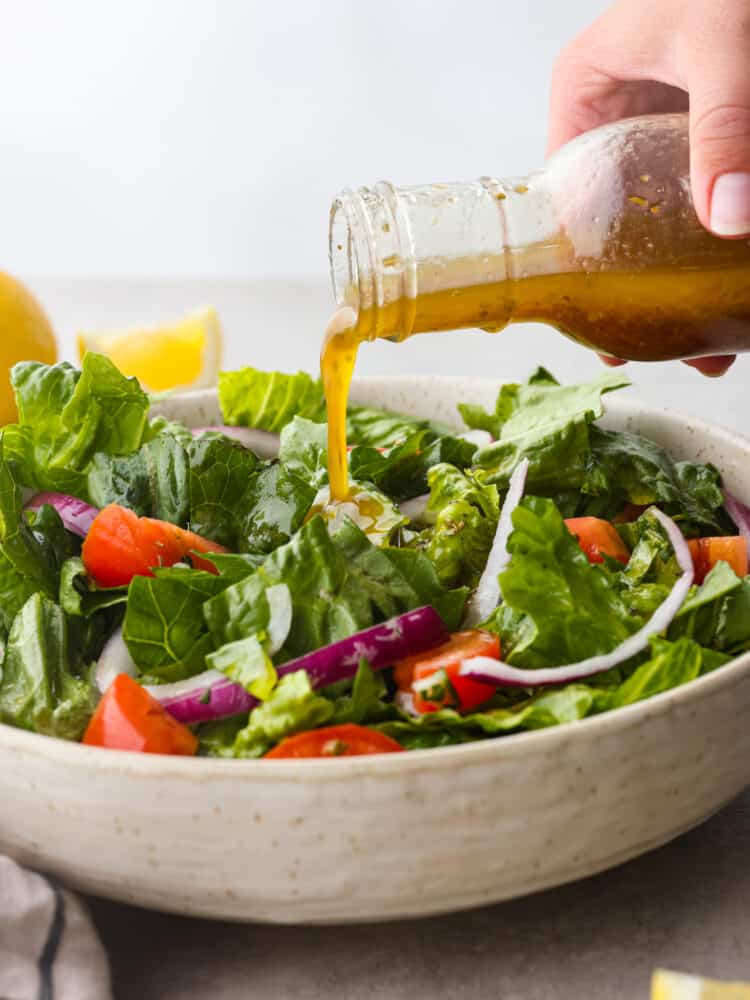 Italian salad dressing being poured over a green salad. 