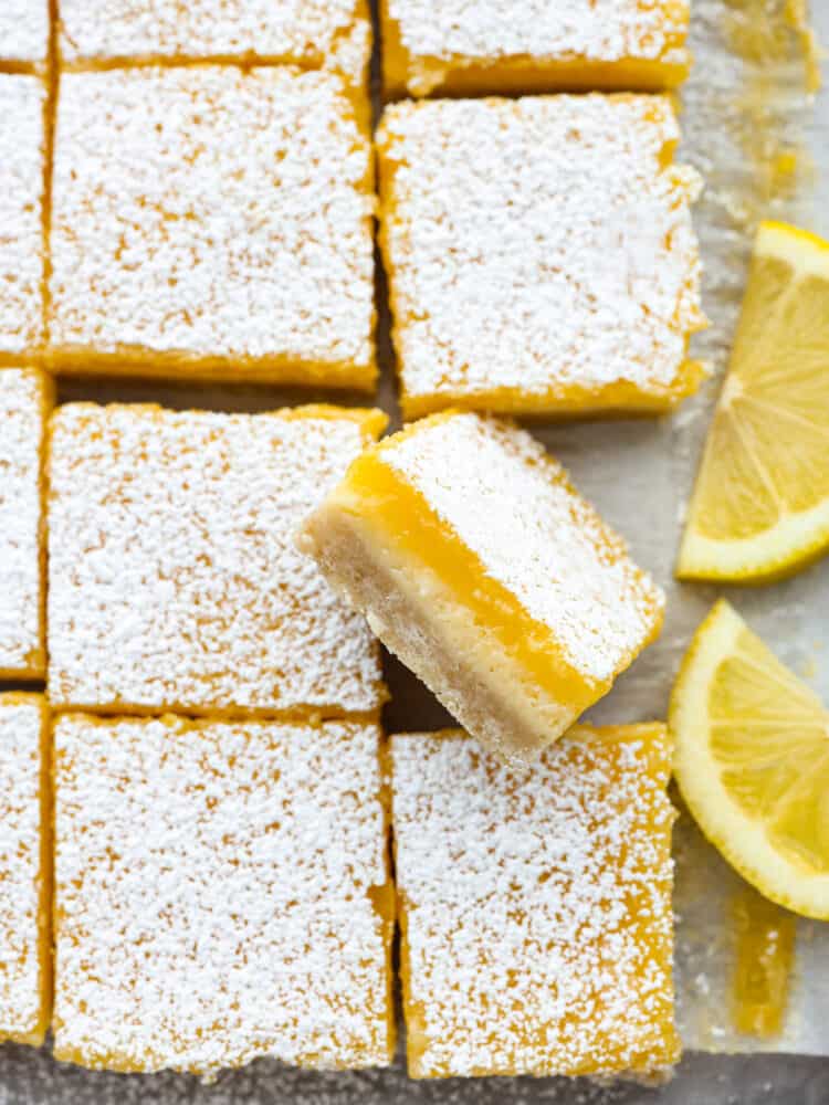 Lemon cheesecake bars on parchment paper. One is turned to the side so that you can see all of the layers. 
