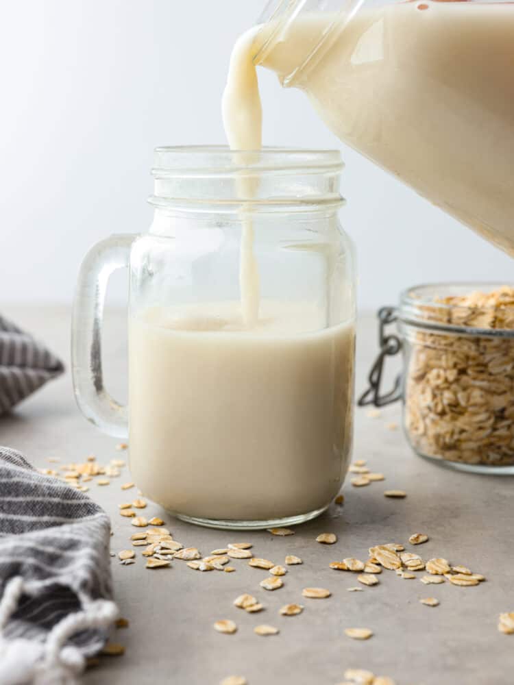 Oat milk being poured into a glass jar with a handle.