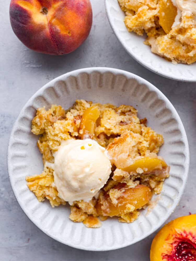 Top-down view of a scoop of peach dump cake in a white bowl served with ice cream.