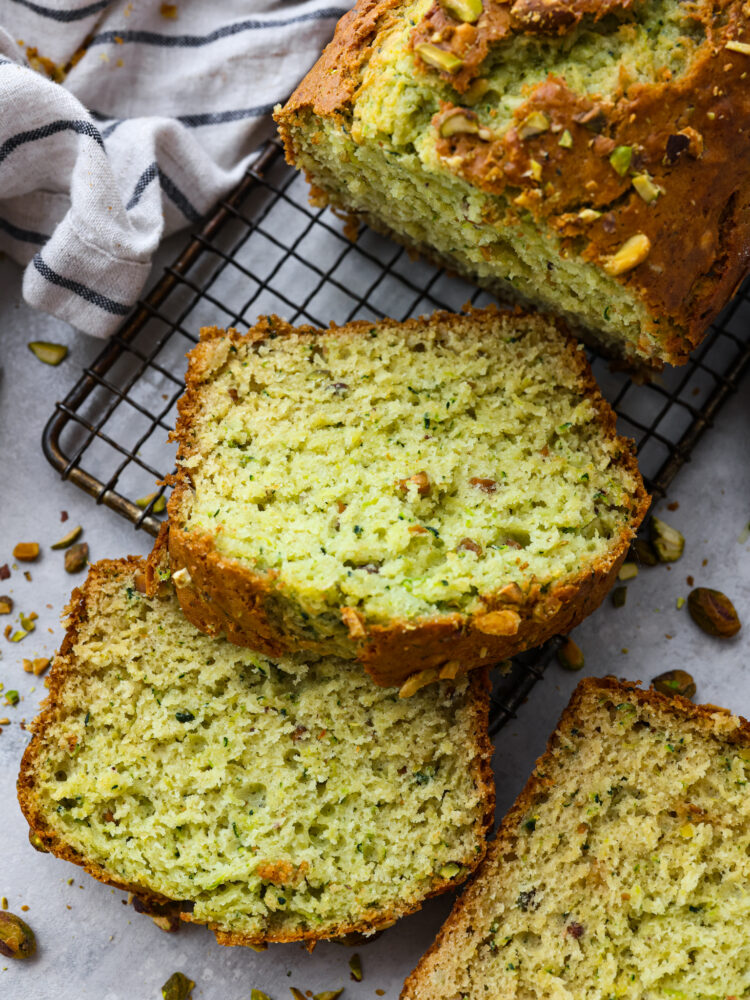 A loaf of pistachio bread on a cooling rack with the end sliced. 