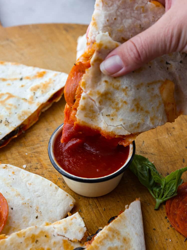 A triangle slice of pizza quesadilla being dipped in some marinara sauce. 