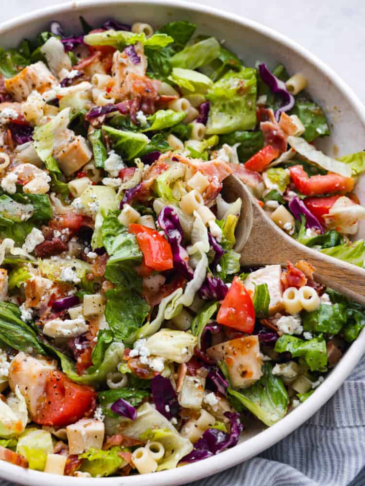 A bowl of Portillo's chopped salad with a wooden spoon in it, ready to serve it. 