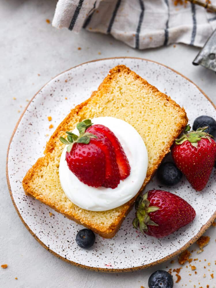 A slice of cake on a stone plate with whipped cream and strawberries.