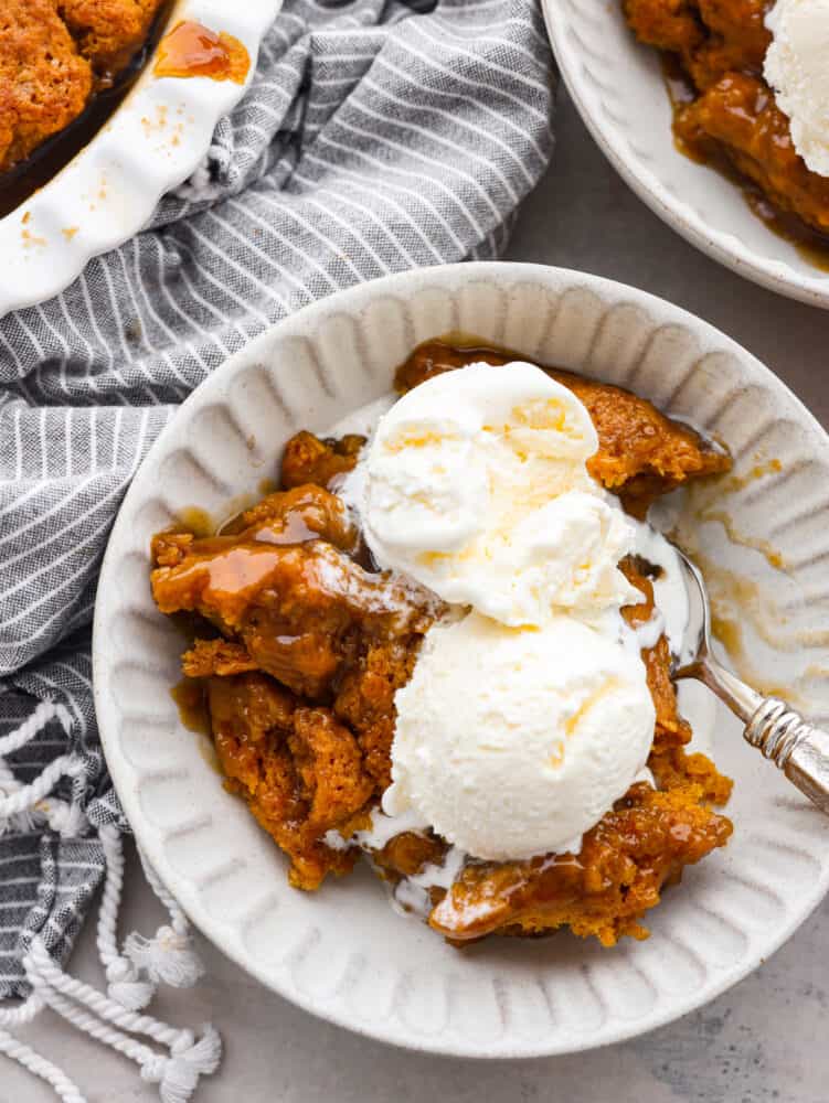 Top-down view of pumpkin pudding cake served in a white bowl with 2 scoops of vanilla ice cream on top.