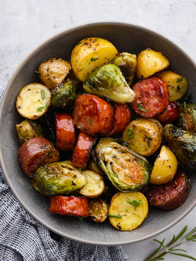 Sausage, Brussels sprouts and potatoes all cooked and seasoned and in a gray bowl. 