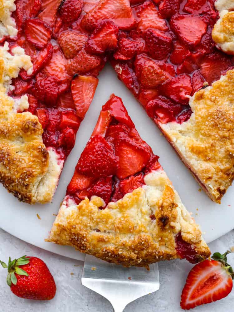 Close up and top view of a slice of galette being served. Fresh strawberries garnished on the side.