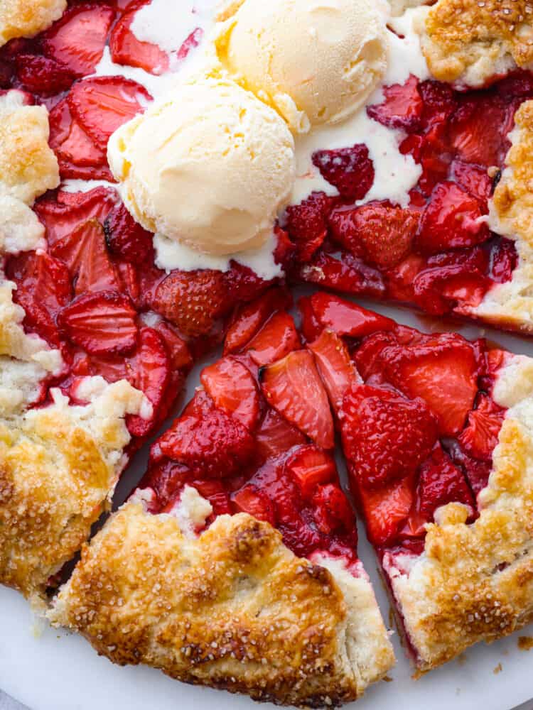 A closeup view of two slices cut out of the whole strawberry galette.  Two scoops of ice cream are on top of the galette and starting to melt.