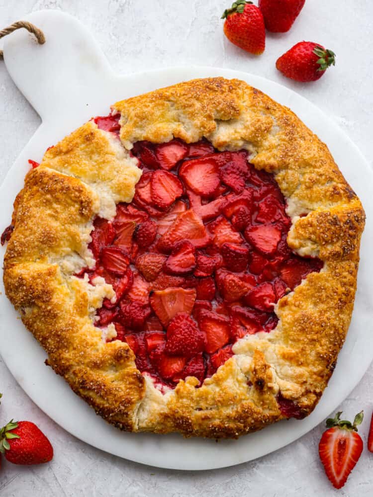 Top view of baked strawberry galette on a marble board.  Fresh whole and halved strawberries scattered beside the galette.