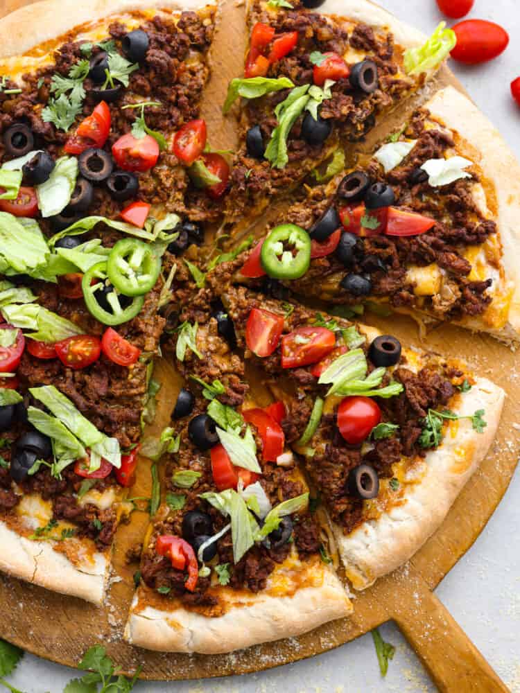 Sliced taco pizza on a wooden serving board.