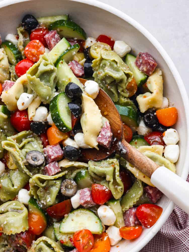 A bowl of Italian tortellini pasta salad with a wooden spoon. 