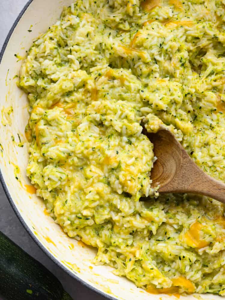 A pan with cheesy zucchini rice with a wooden spoon. 
