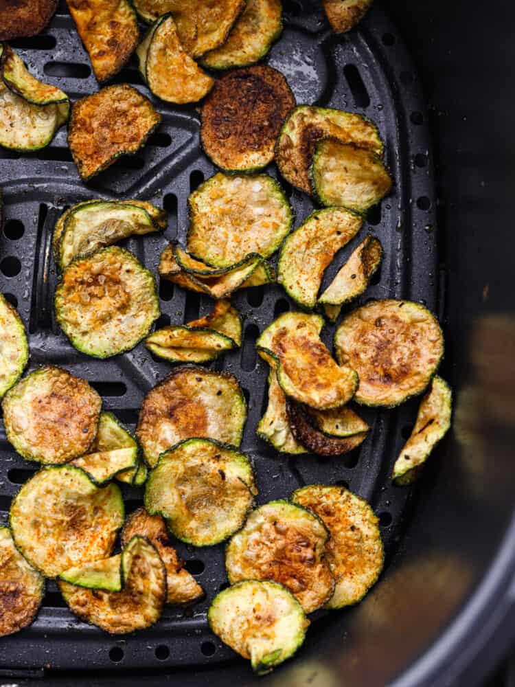 Cooked zucchini chips in the bottom of an air fryer basket.