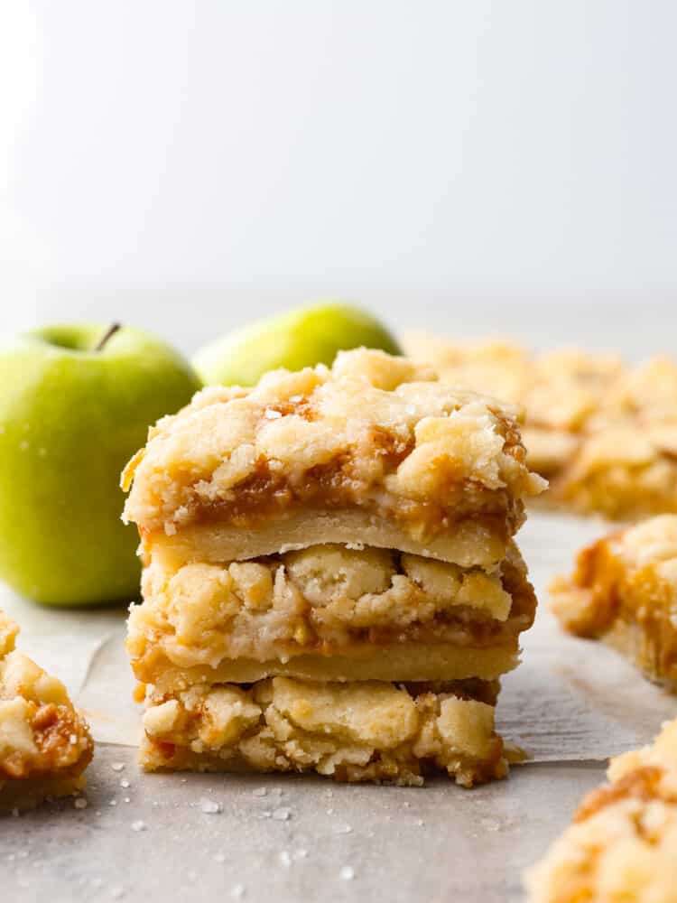 A stack of caramel apple bars on the counter with some green apples in the background. 
