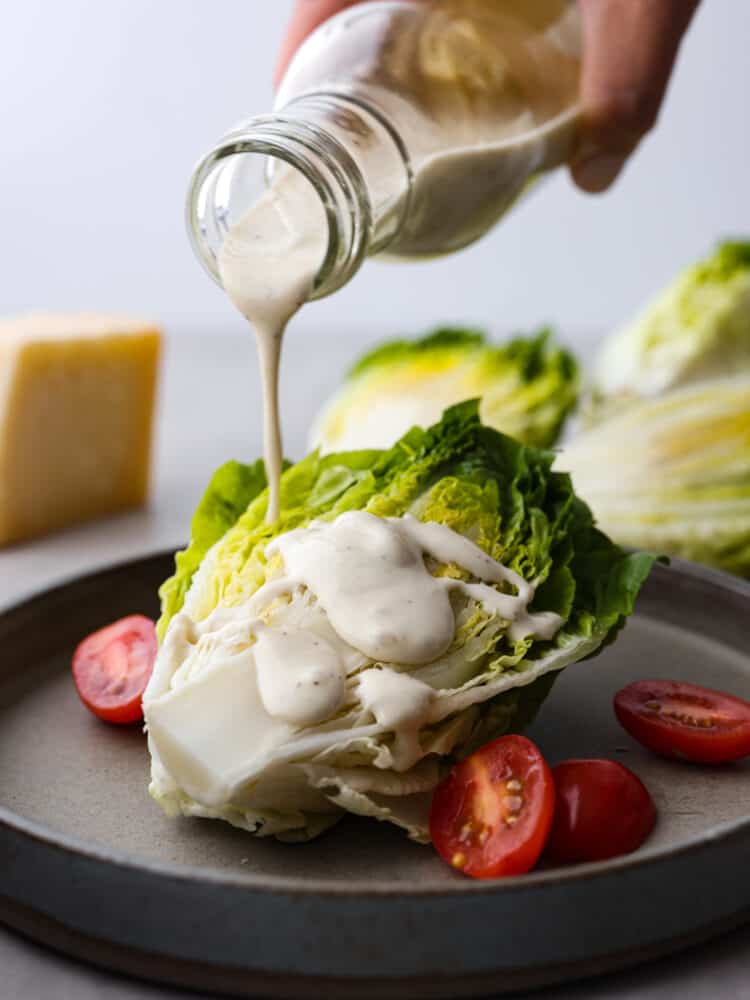 Salad dressing being poured onto a wedge of lettuce. 