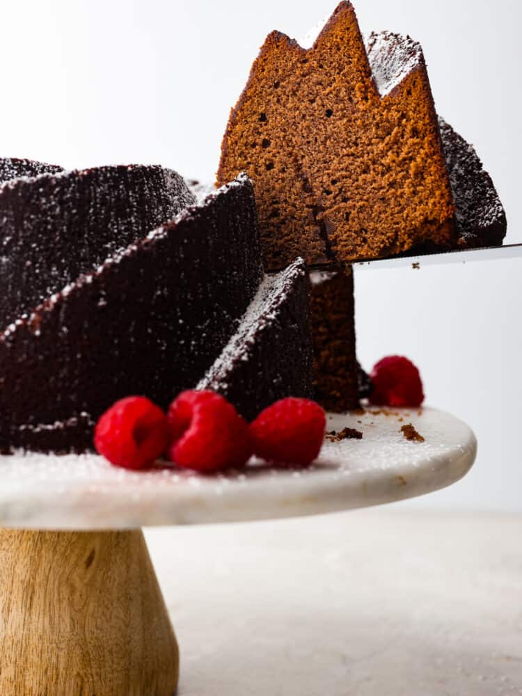 The side view of a chocolate pound cake on a cake stand with a slice being taken out. 