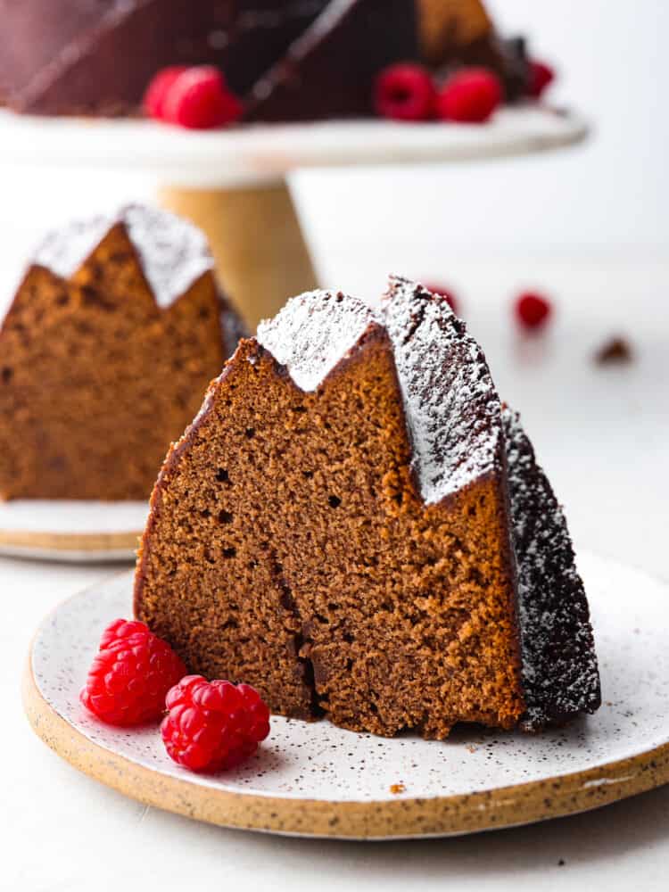 A slice of chocolate pound cake with some raspberries next to it, on a plate. 