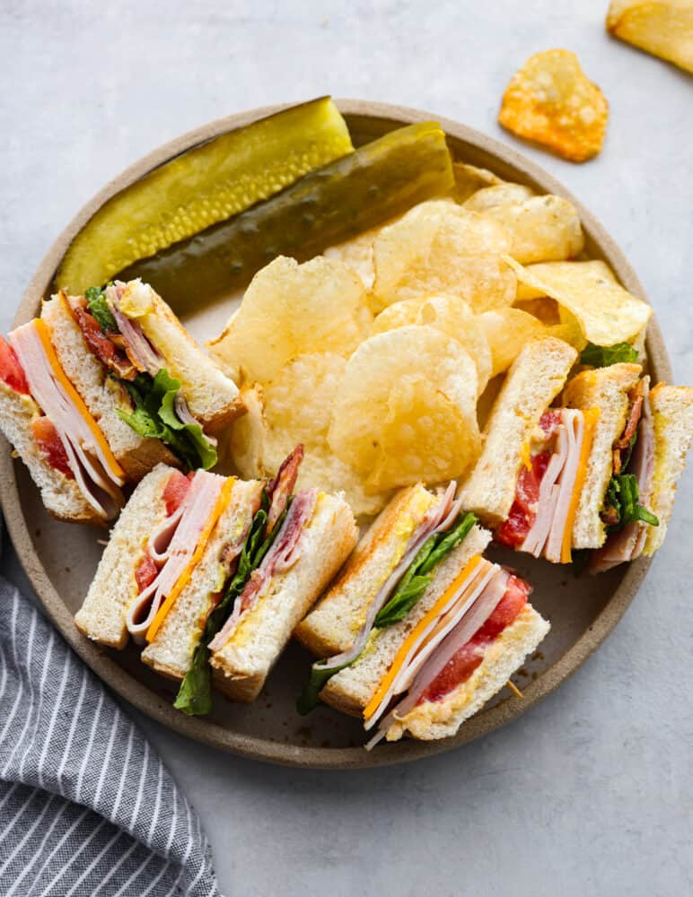 4 club sandwiches served alongside pickles and potato chips.