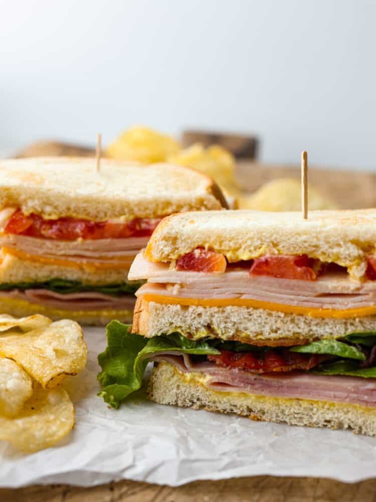 Front view of 2 club sandwiches filled with meat, cheese, and vegetables, held together by toothpicks.