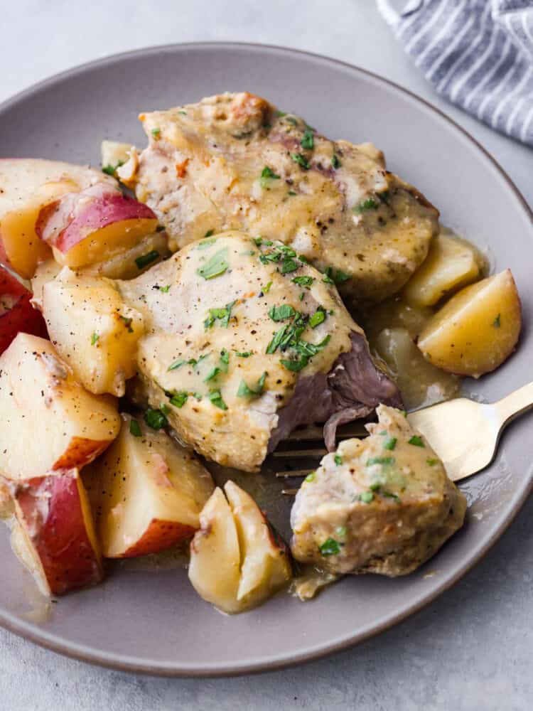 Closeup of ranch pork chops and potatoes served on a gray plate. The pork chop has a slice cut out of it.