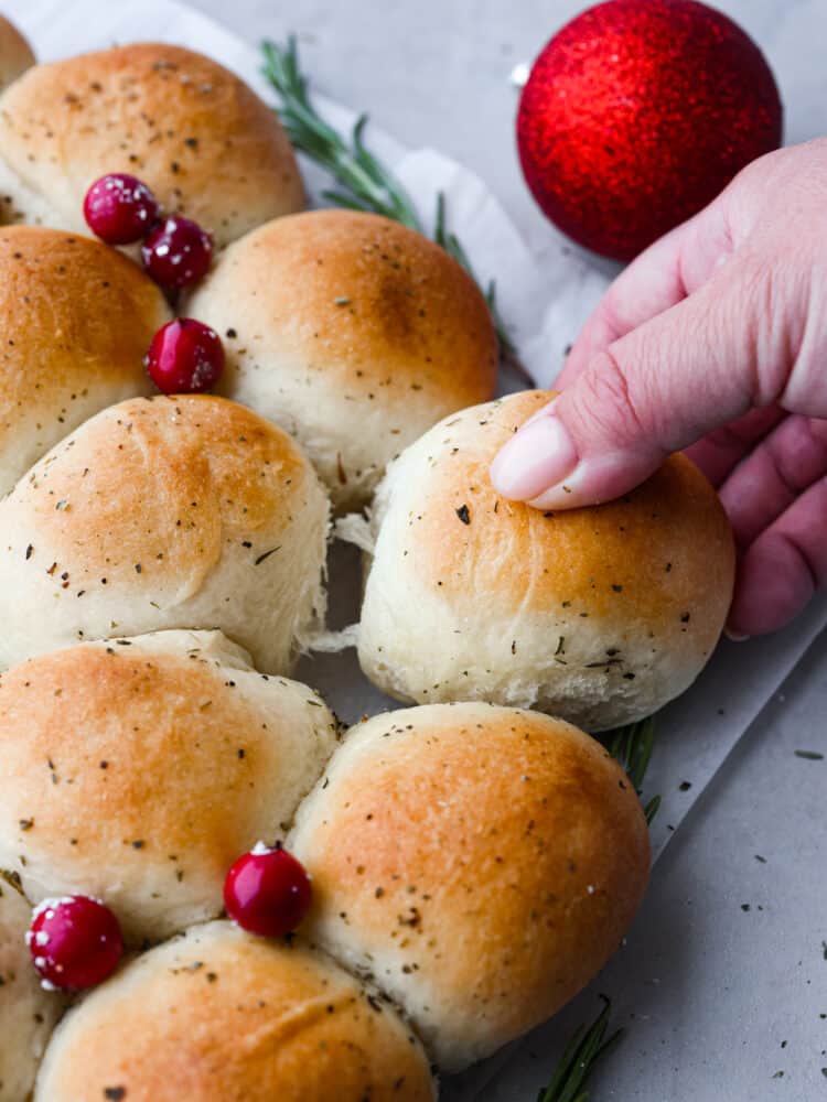 A close up of dinner roll wreath with a hand grabbing one of the rolls.