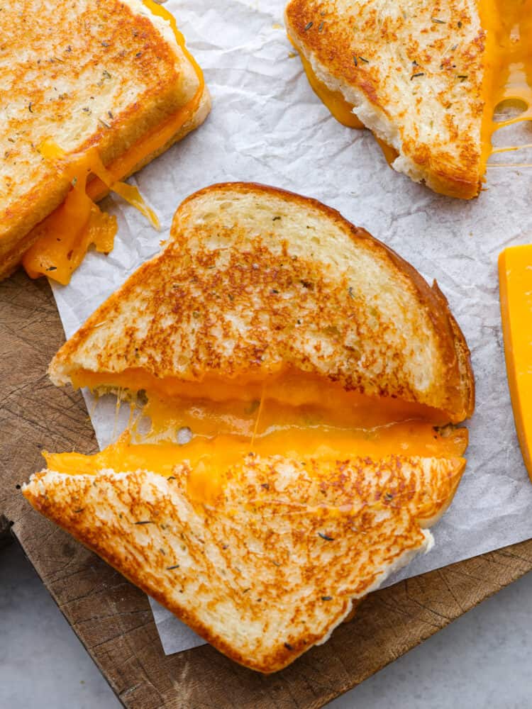 A grilled cheese sandwich on parchment paper, cut on the diagonal and pulled apart about an inch so that you can see the melted cheese inside. 