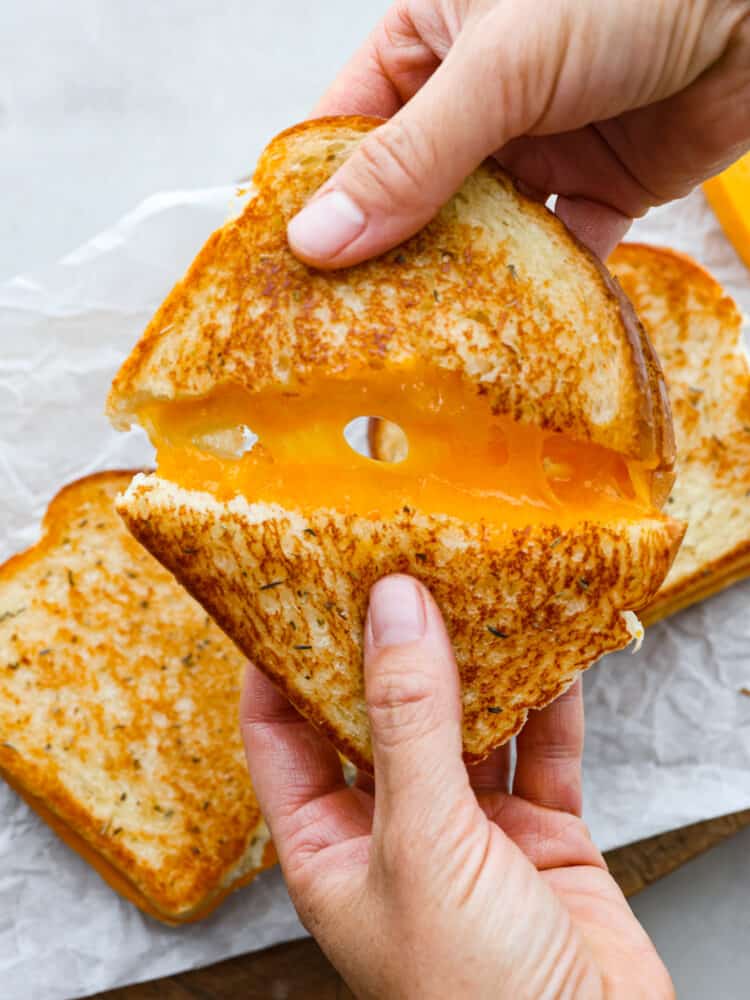 A grilled cheese sandwich cut in half and being pulled apart. 