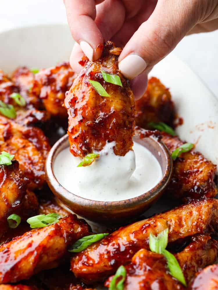 A close up of a wing being dipped into ranch dressing. 