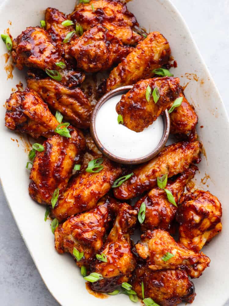 A platter of wings with one being dipped into ranch dressing. 