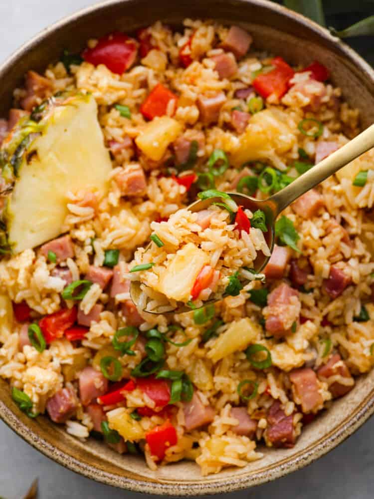 A close up of a spoonful of Hawaiian fried rice with a bowl of fried rice blurred in the background. 