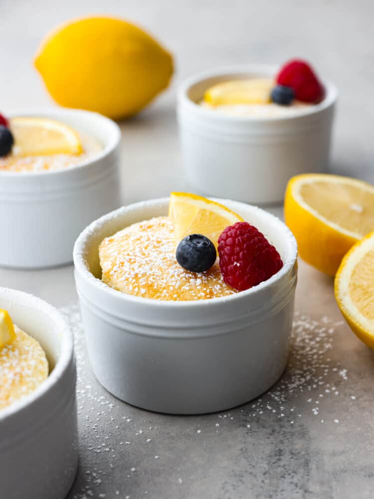 Lemon pudding cake in individual ramekins with a lemon slice, raspberry and blueberry on top. 