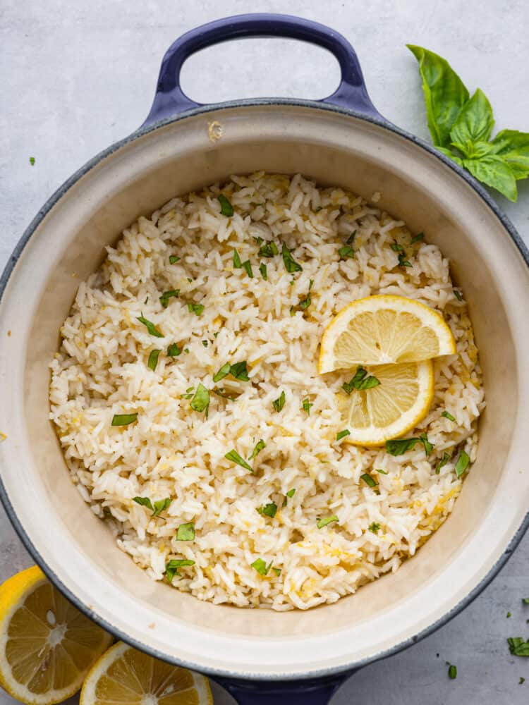 Top-down view of cooked lemon rice in a blue pot, garnished with chopped basil and lemon slices.