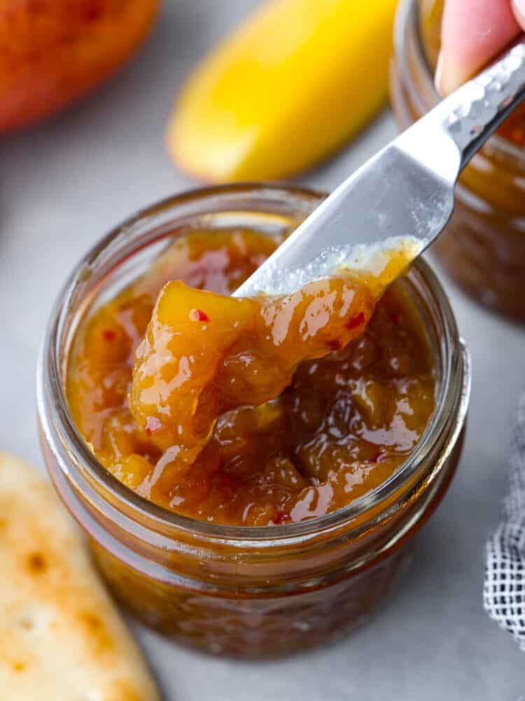 A jar of mango chutney with a knife getting some out. 