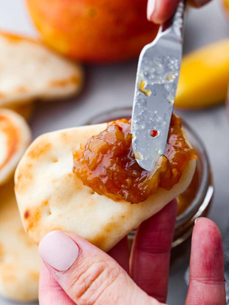 A knife spreading some mango chutney on a small piece of naan bread. 