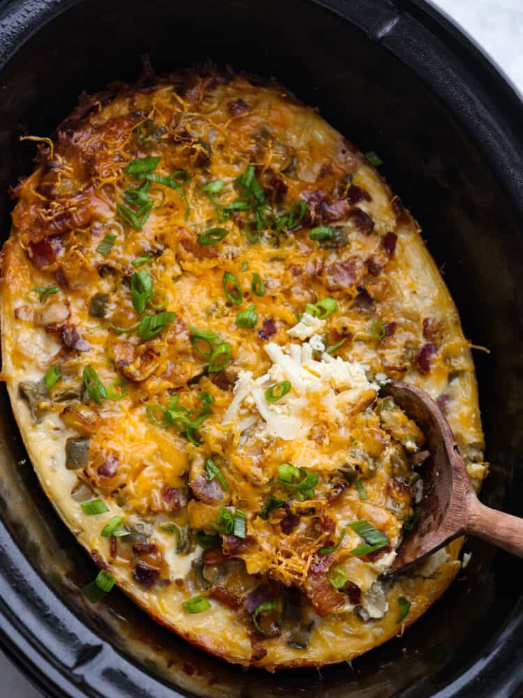 Breakfast casserole in a slow cooker with a wooden spoon sticking out. 