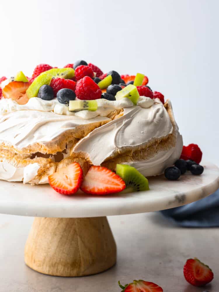 Pavlova on a cake stand topped with fresh fruit. 