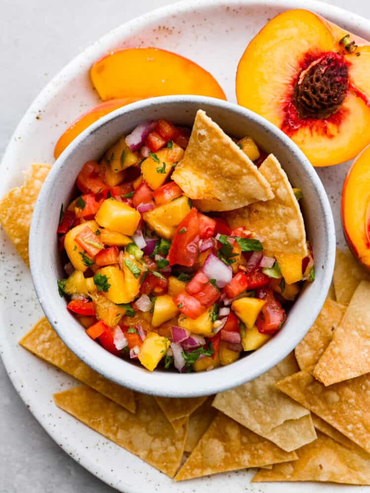 The top view of a bowl of peach salsa with tortilla chips. 