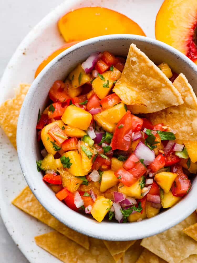A close up of the top of a bowl filled with peach salsa and tortilla chips. 