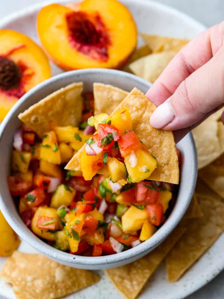 A tortilla chips scooping out peach salsa. 