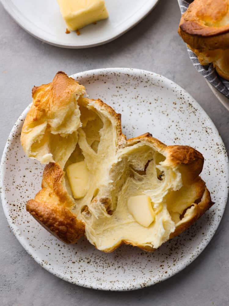 A popover torn in half with butter added on a white speckled plate.