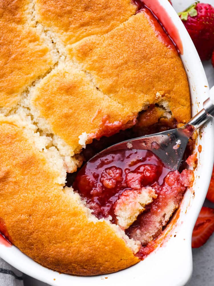 Strawberry cobbler in a baking dish with a large spoon scooping some out. 