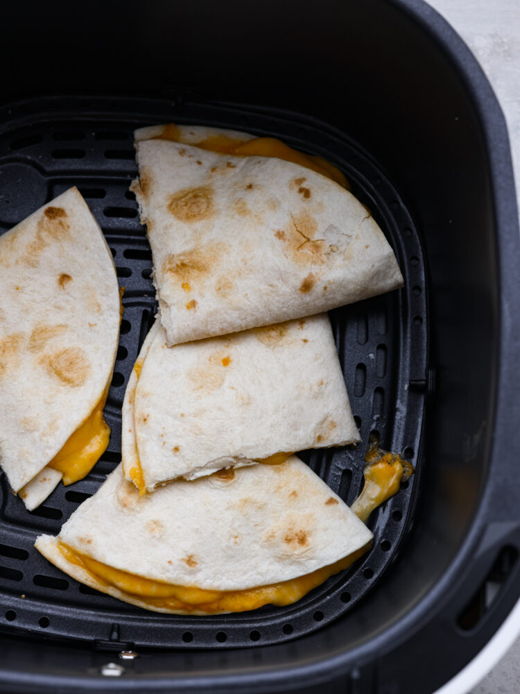 Top view of air fryer quesadilla in a black air fryer basket.  The quesadilla is cut into triangles with melted cheese oozing out.