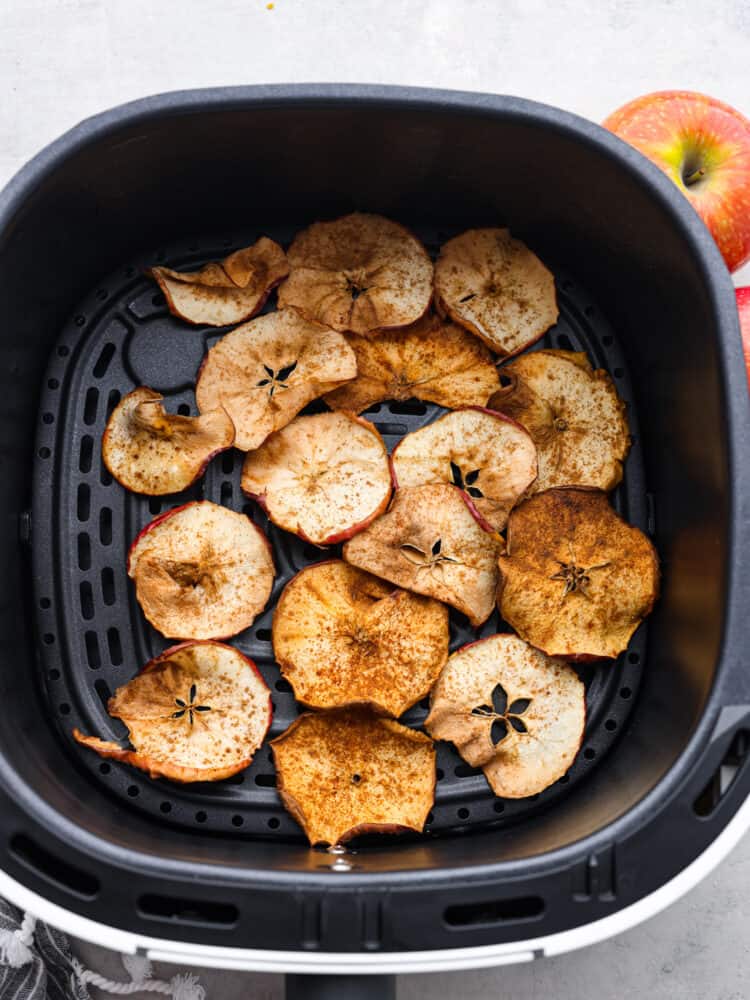 Top view of spiced apple chips in the air fryer.  Red apples are placed next the air fryer.