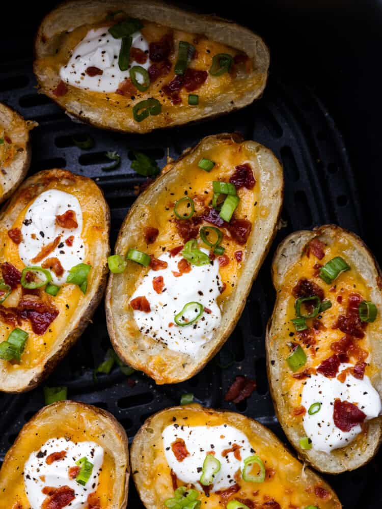 Close up view of air fryer potato skins  in an air fryer garnished with sour cream, green onions, and bacon.